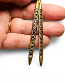 Gold earrings with gemstones held in a hand against a white background