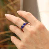 Hand wearing a purple ring with a blurred natural background