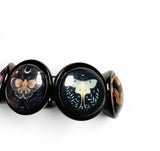 A close-up of a black beaded bracelet featuring round glossy beads with detailed fantasy illustrations of butterflies, moths, and crescent moons on a white background.