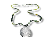 Necklace with green beads and a silver pendant on a white background. Necklace with green and black beads and a silver Myan calendar pendant