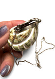 Shell-shaped jewelry box with a chain held by a hand on a white background