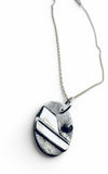 A silver pendant necklace featuring a textured finish, a polished silver diagonal stripe, and a small black circular accent, shown on a white background.