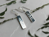 Moon Phase Earrings - silver metal cut out of a moon phase design -vertical design -sterling french hook earwires. on background with leaf design