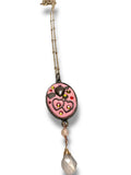 Necklace with a pink pendant featuring heart designs on a white background